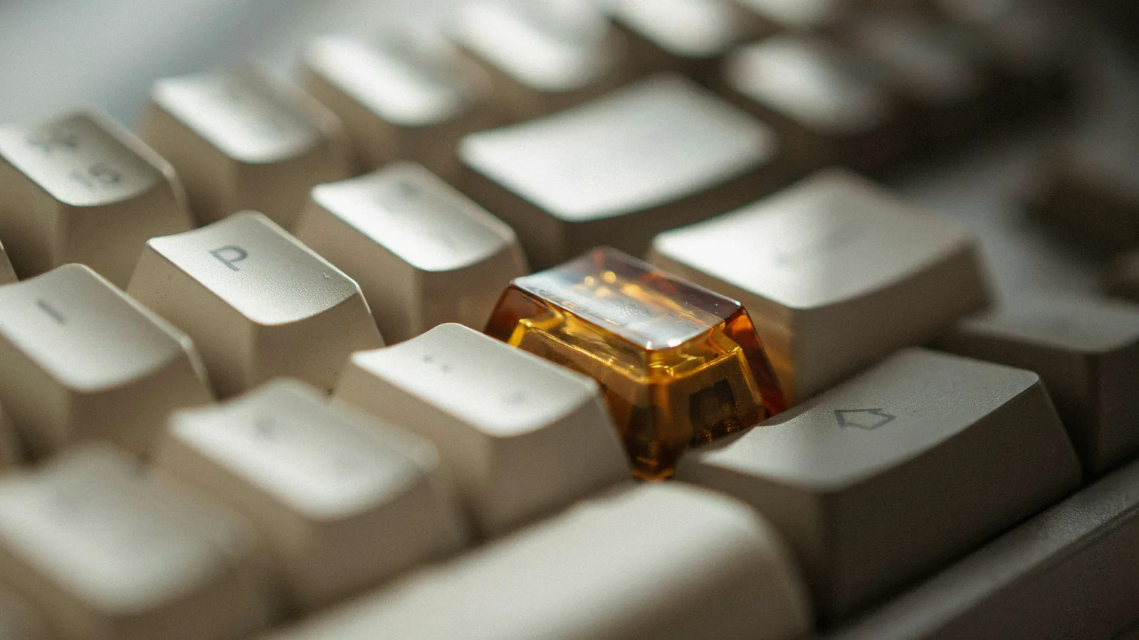 Nahaufnahme mechanischer Tastatur-Keycaps in Beige mit einer durchscheinenden bernsteinfarbenen Akzent-Taste